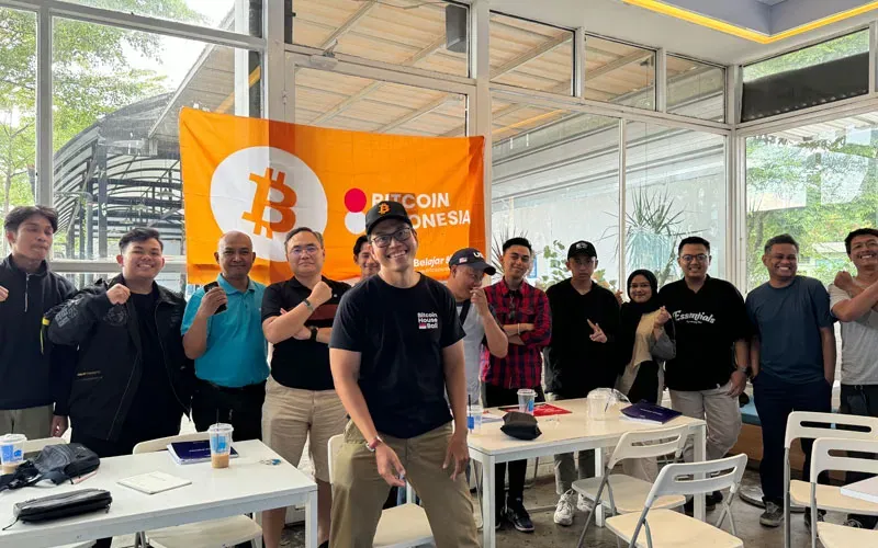 A My First Bitcoin community gathering: people stand together in front of an orange Bitcoin banner